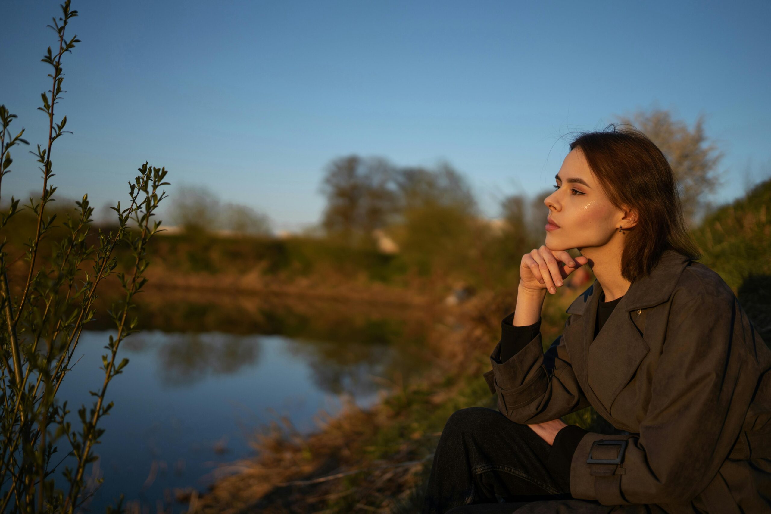 A woman sitting by a lakeside, contemplating nature during sunset.